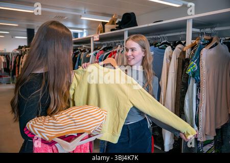 Zwei junge Frauen, die in Second-Hand-Bekleidungsgeschäft ihre Kleidung durchsuchen Stockfoto