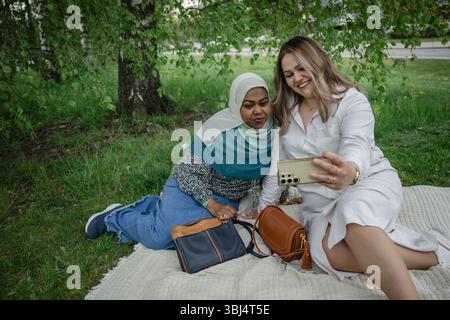 Zwei ethnisch unterschiedliche Frauen machen ein Selfie auf Picknickdecke Stockfoto