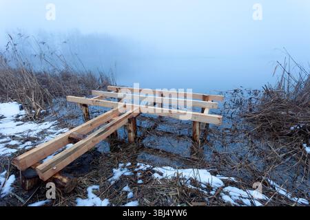 Bau eines neuen Holzsteges am Ufer eines nebeligen Sees Stockfoto