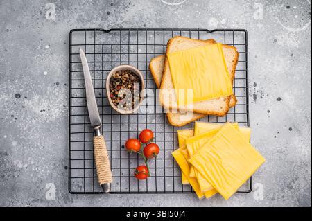 Quadratische Scheiben von verarbeitetem Cheddar-Käse in Einzelverpackung aus Kunststoff. Grauer Hintergrund. Draufsicht. Stockfoto
