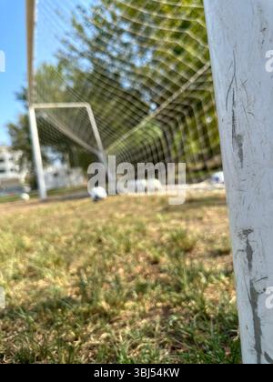 Fußball auf grünem Gras in der Nähe des Tornetzes unter sonnigem Himmel, Nahaufnahme des Fußballfeldes Stockfoto