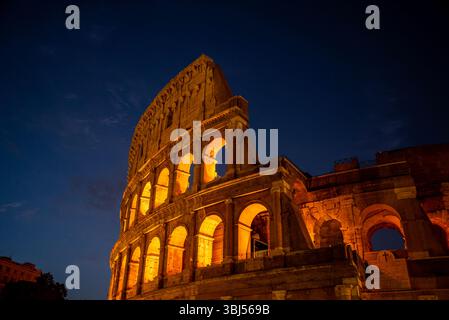Das Kolosseum in Rom, Italien, leuchtet orange unter der Nachtbeleuchtung, vor einem dunkelblauen, wolkenlosen Himmel, und hebt seine berühmte antike Architektur hervor. Stockfoto