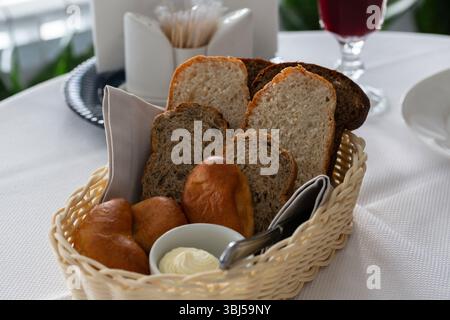 Brot im Korb. Weiß-schwarz geschnittenes Brot, Butter und Kuchen in einem Korb auf dem Tisch im Restaurant Stockfoto