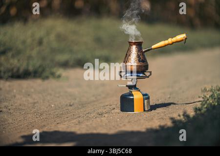 Türkische Kaffeekanne mit Holzgriff auf einem tragbaren Gasherd auf der Landstraße. Im Freien Stockfoto