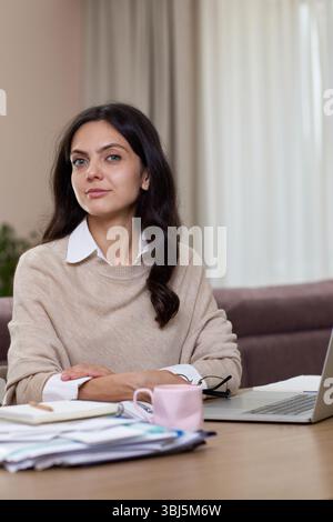 Porträt einer ruhigen Frau, die zu Hause in die Kamera schaut. Erfolgreiche Frau, die zu Hause arbeitet. Stockfoto