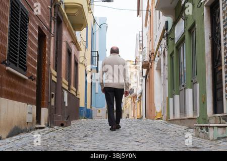 Ein älterer Mann, der eine enge portugiesische Straße hinunterläuft, von hinten gesehen. Stockfoto