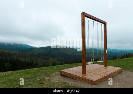 Dieses Bild zeigt eine atemberaubende Schaukel auf einem Berghügel mit atemberaubendem Blick auf üppige Wälder und sanfte Hügel unter bewölktem Himmel Stockfoto