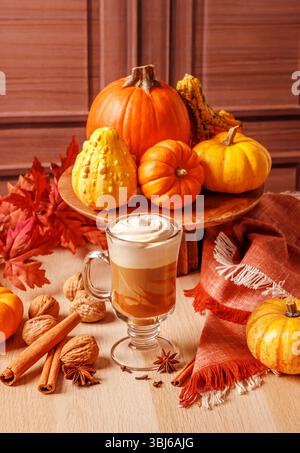 Ein Herbstthema mit einem Latte mit Schlagsahne, umgeben von Kürbissen, Kürbissen, Zimtstangen, Walnüssen, Sternanis, Nelken und Herbst Stockfoto