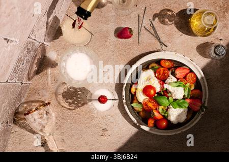 Direkt über Caprese-Salat mit Erdbeeren, bei hartem Licht wird Prosecco in ein Glas gegossen Stockfoto