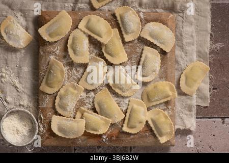 Direkt über hausgemachten Ravioli auf Holzbrett, mit Sichter und Mehl, fertig zum Kochen Stockfoto