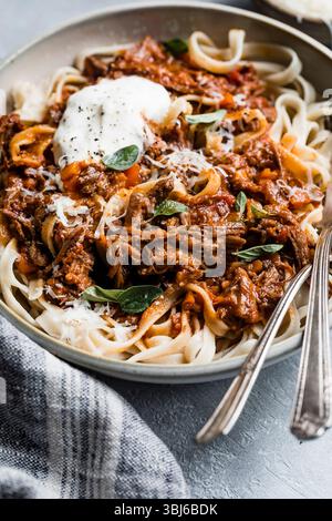 Ein Teller mit Nudeln, garniert mit einer reichhaltigen Fleischsauce, garniert mit frischen Kräutern und einem Klecks Sauerrahm. Stockfoto