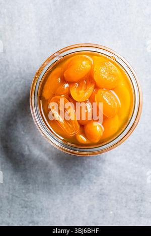 Draufsicht eines Gefäßes, gefüllt mit konservierten Kumquats in Sirup auf grauem Hintergrund. Stockfoto