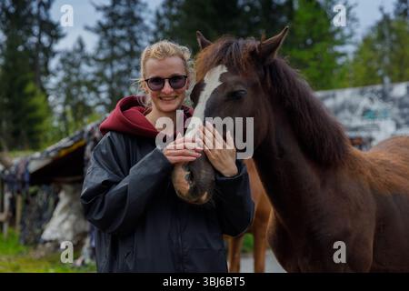 In dieser herzerwärmenden Szene posiert eine lächelnde junge Frau mit einem sanften Pferd, zeigt ihre Verbundenheit vor einer ruhigen natürlichen Kulisse und reflektiert ein d Stockfoto