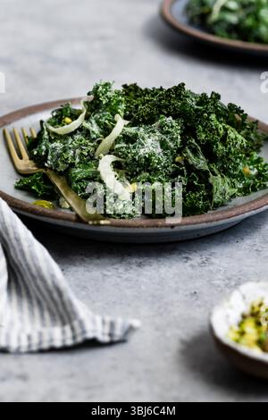 Ein Teller Grünkohl-Salat mit cremigem Dressing und Fenchel in Scheiben, begleitet von einer goldenen Gabel auf grauer Oberfläche. Stockfoto