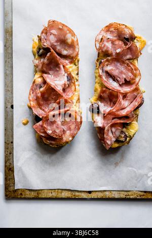 Zwei offene Sandwiches mit Salamischeiben und geschmolzenem Käse auf einem Backblech. Stockfoto