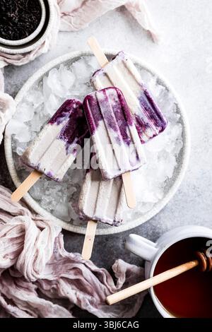 Ein Teller mit Eis gefüllt mit violetten und weißen Stielen neben einer Tasse Tee und einer Schüssel getrockneter Kräuter. Stockfoto