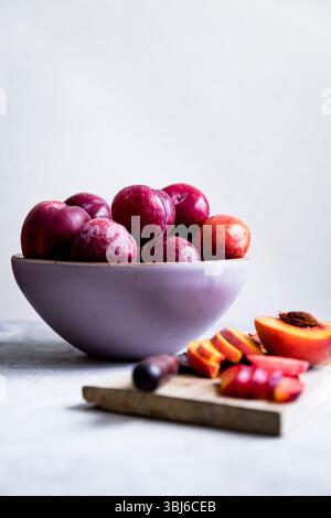 Eine Schüssel mit frischen Pflaumen mit geschnittenen Pfirsichen auf einem Holzbrett. Stockfoto