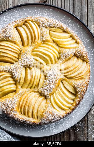 Ein Apfelkuchen mit Puderzucker wird auf einem Holztisch ausgestellt. Stockfoto