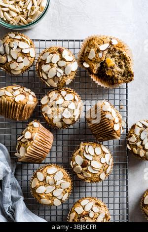Muffins mit Mandelstopfen, die auf einem Gitterrost mit einer Schüssel Mandelsplitter in der Nähe abkühlen. Stockfoto