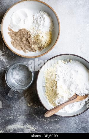 Zwei Schüsseln mit verschiedenen Mehlsorten und ein Messbecher aus Glas auf strukturierter Oberfläche. Stockfoto
