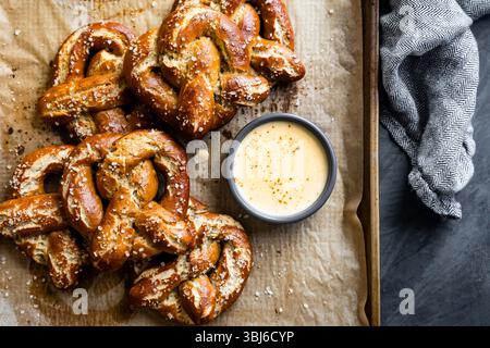Ein Tablett mit frisch gebackenen Brezeln mit grobem Salz und einer Schüssel Käse-Dip. Stockfoto