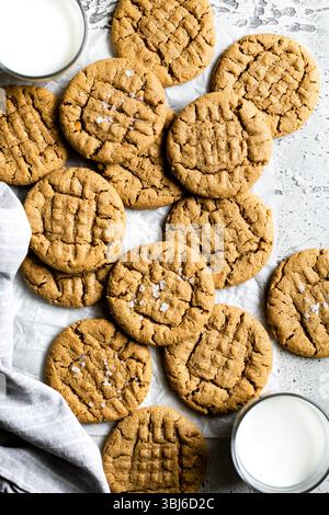 Eine Portion frisch gebackener Erdnussbutter-Kekse mit Kreuzmuster, bestreut mit Meersalz und begleitet von Gläsern Milch. Stockfoto
