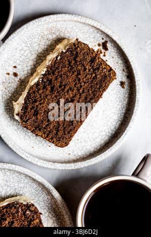 Ein Stück Schokoladenkuchen mit Zuckerguss wird auf einem strukturierten Teller serviert, begleitet von einer Tasse schwarzen Kaffee. Stockfoto