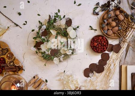 Flaches Legen eines fertigen handgefertigten getrockneten Blumenkranzes auf einem hellen Holztisch, umgeben von Bastelmaterialien wie getrockneten Blumen, Garn Stockfoto