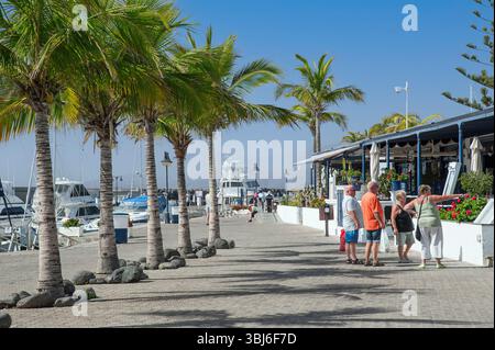 Puerto Calero mit Palmen und Yachthafen, touristische Gruppe von Freunden, die sich das Menü vor dem Restaurant Lanzarote im Freien ansehen Stockfoto