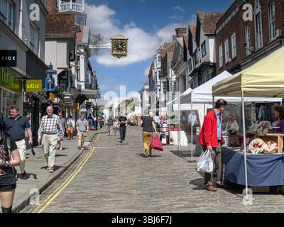Guildford Market Day historische Kopfsteinpflasterstraße, Wahrzeichen Uhr und Shopper, mit Sommer lokalen Kunst- und Kunsthandwerksstand Guildford Surrey UK Stockfoto