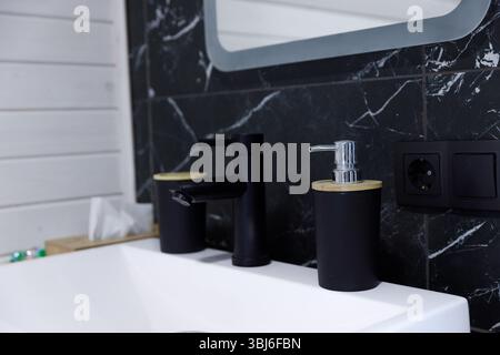 Eine moderne und elegante Badezimmerablage mit stilvollen Accessoires, darunter ein eleganter Wasserhahn und ein schicker Seifenspender in Schwarz und Holz Stockfoto