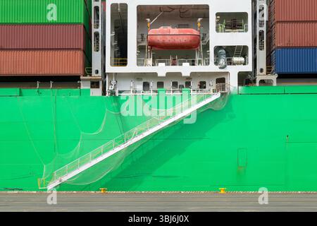Ein belebtes, grünes Frachtschiff legte an und zeigte seinen Zugangsgang, ein Sicherheitsnetz und ein rotes Rettungsfloß. Einzelheiten zur maritimen Logistik. Stockfoto