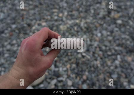 Ein flacher Stein in der Hand eines Mannes auf dem Hintergrund eines Strandes Stockfoto
