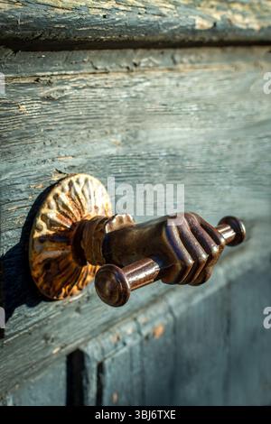 Ein markanter Türgriff, der einem Handgriff ähnelt, fasst eine rustikale Holztür mit komplizierten Details und einer charmanten Patina. Frankreich Stockfoto