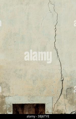 Eine gerissene Wandoberfläche zeigt den Zeitverlauf mit sichtbarem Verschleiß. Die Textur hebt Licht- und Schattenspiel hervor und weist auf eine städtische Umgebung hin. Stockfoto