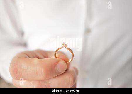 Diamantgoldring. Schmuck. Nahaufnahme der Hand des Mannes, der einen eleganten Diamantgoldring hält. Verlobungsfotos, Heiratsantrag. Stockfoto