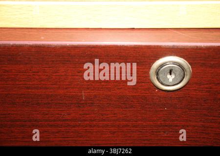 Nahansicht einer Holzschublade mit einem runden Metallschloss, das in der Oberfläche integriert ist. Das Holz hat eine polierte, rotbraune Oberfläche. Stockfoto