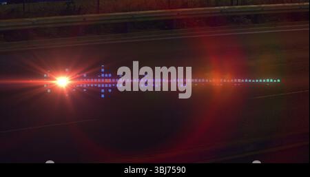 Fahrzeugscheinwerfer, die bei Nacht Lichtreflexe mit farbigen Reflexen auf der Straße erzeugen, mit Schutzgeländer Stockfoto