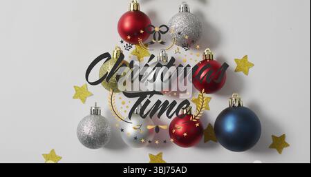 Weihnachtskugeln mit Weihnachtsschriftzug und Sternkonfetti auf weißer Tischplatte Stockfoto