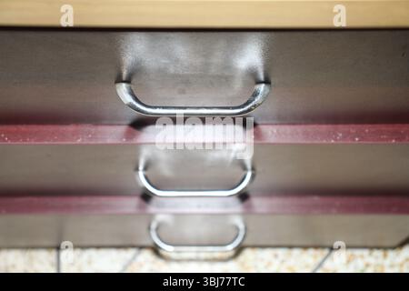 Die drei Griffe der Metallschublade sind vertikal auf einem Schrank ausgerichtet. Die Schubladen haben eine glatte, reflektierende Oberfläche mit gebürstetem Metall. Stockfoto