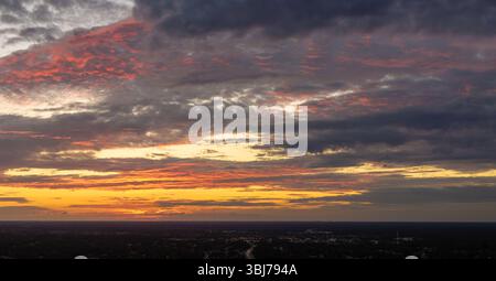 Farbenfroher Sonnenuntergang über dem ländlichen Gebiet. Untergehende Sonne hinter leuchtenden orangen und gelben Wolken Stockfoto