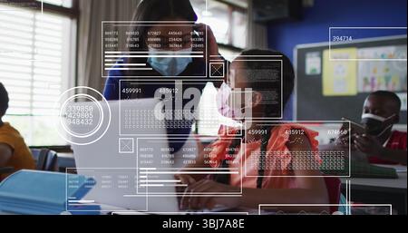 Weibliche Lehrerin mit Schutzmaske, die sitzende Schülerin im Klassenzimmer mit Laptops unterstützt Stockfoto