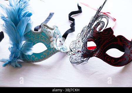 Hellblaue und schwarz rote Karnevalsmasken mit blauen und schwarzen Federn auf hellrosa Hintergrund, dekoratives Accessoire Stockfoto