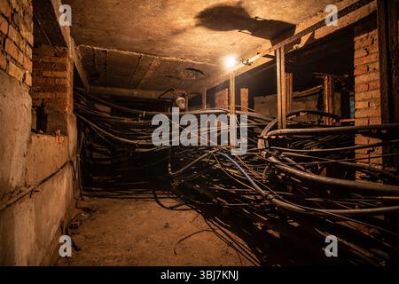 Ein alter unterirdischer Kabeltunnel oder Keller mit Kabeln mit Wolframlampen-Beleuchtung. Stockfoto
