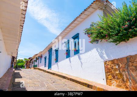 Barichara, Santander, Kolumbien, 11. Oktober 2024. Flacher Blick auf eine kopfsteingepflasterte Straße mit einem weißen Kolonialhaus mit hellblauen Fenstern, Ty Stockfoto