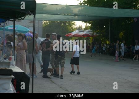 Am ersten Tag des jährlichen Moto Rock fest in Ruse, Bulgarien, am 13. Juni 2025, treffen sich die Menschen im Abendschatten. Die Veranstaltung bringt Radfahrer, Familien und Zuschauer unter großen Netzen und Markenschirmen zusammen. In der Nähe von Imbissständen und Sitzbereichen im Freien interagieren verschiedene Teilnehmer – darunter Männer in Bikerwesten, Kinder und Frauen mit einem Geburtstagsballon. In der Ferne parken Motorräder unter Zelten, während Kinder spielen und Familien sich unterhalten. Die entspannte und gemeinschaftliche Atmosphäre spiegelt den offenen Geist dieses dreitägigen internationalen Motorrads und der Rockmusik wider Stockfoto
