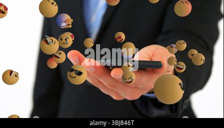 Die Hand eines Geschäftsmannes in schwarzem Anzug, der das Smartphone im Studio hält, mit schwimmenden Emoji-Symbolen Stockfoto