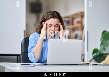 Gestresste junge Angestellte, die den Kopf berührt und Kopfschmerzen fühlt, Müdigkeit bei der Arbeit. Stockfoto