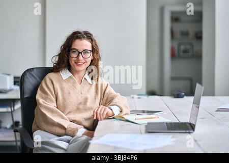 Junge glückliche professionelle Geschäftsfrau sitzt am Schreibtisch, Porträt. Stockfoto