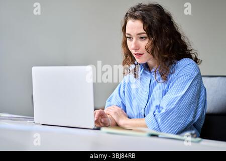 Junge Geschäftsfrau, die am Schreibtisch sitzt und an einem Laptop arbeitet. Stockfoto